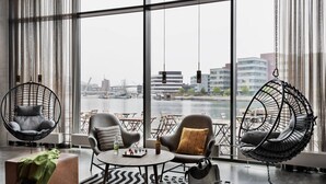 Una habitación moderna con ventanas amplias, vista al río y asientos al aire libre junto a la ventana.