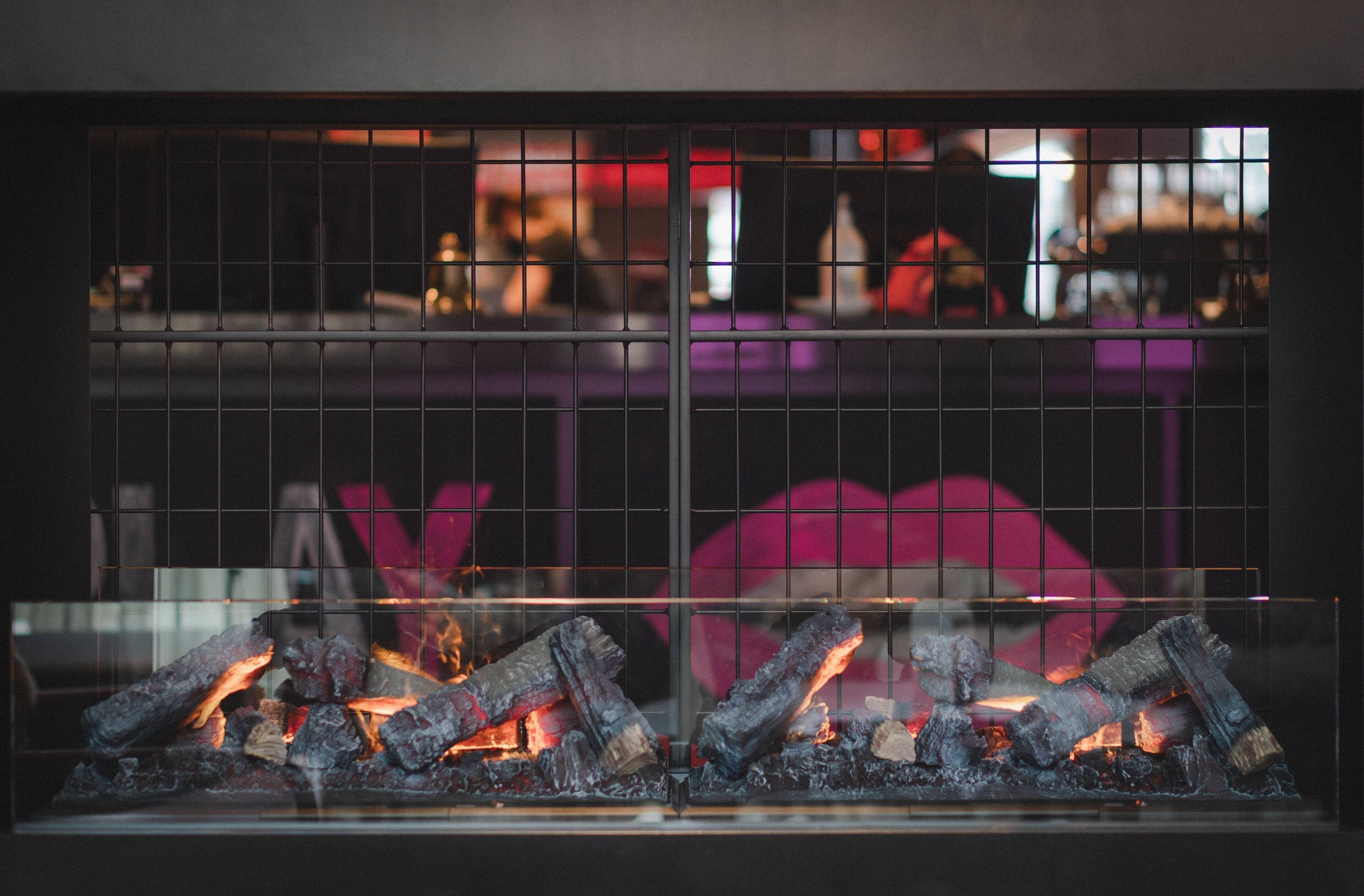 Une cheminée où brûlent des bûches, vue à travers une grille métallique.
