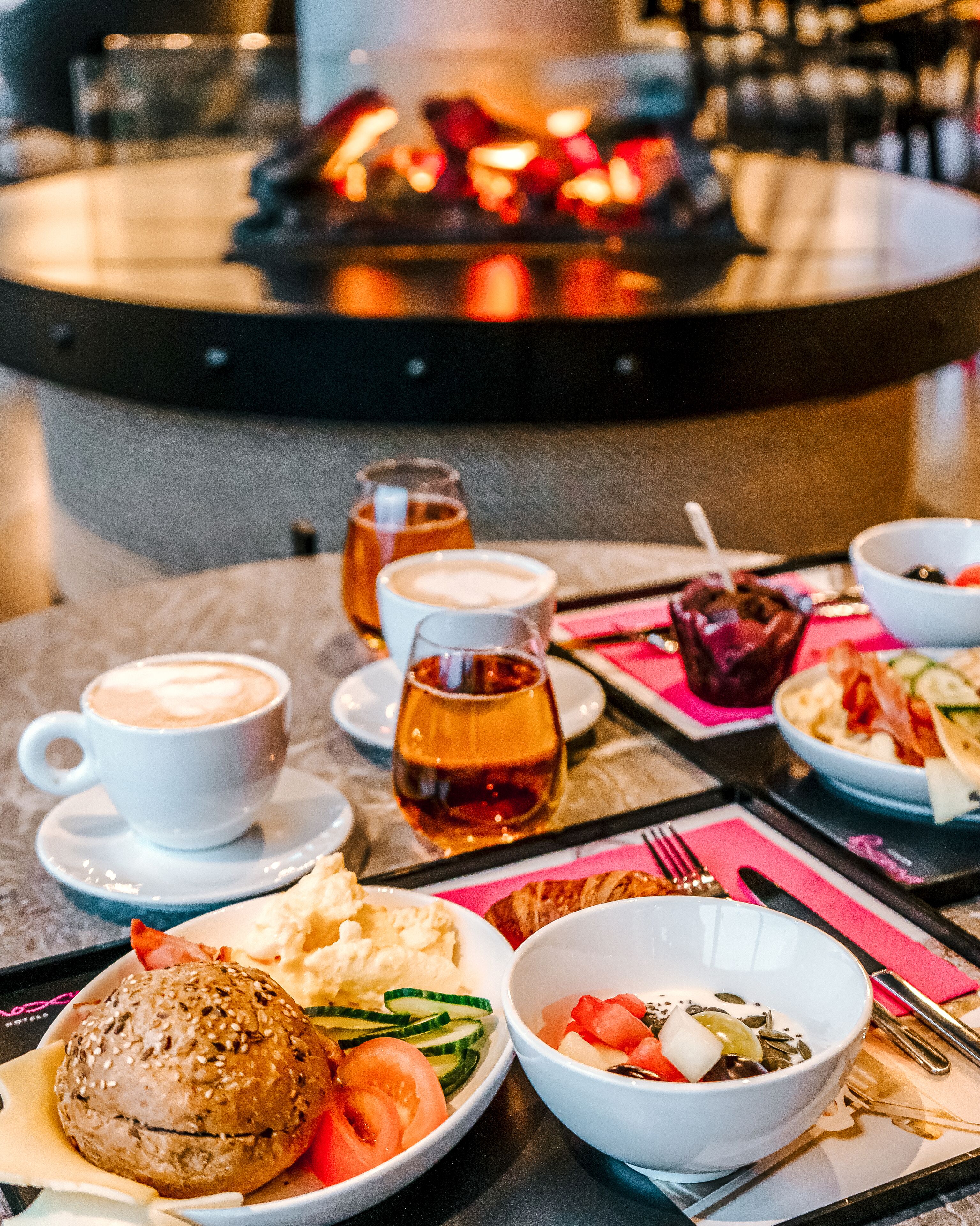 A dining table with various dishes, including a burger, salad, and soup, along with cups of coffee and a glass of tea.