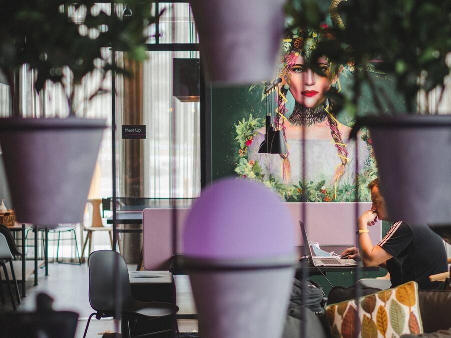 Un interior moderno con plantas colgantes, un mural y una persona trabajando en un ordenador portátil.
