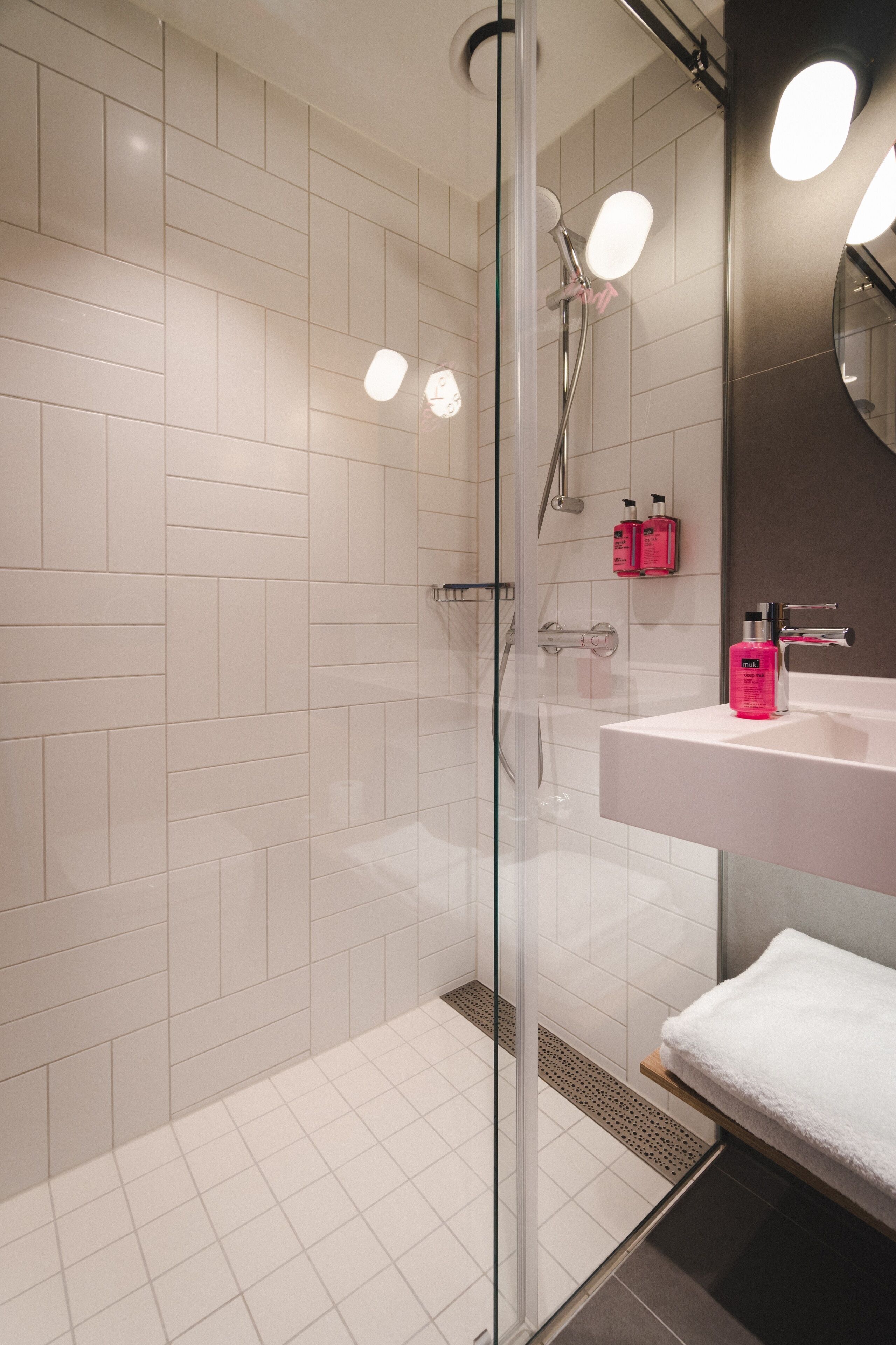 Un baño moderno con cabina de ducha de vidrio, azulejos blancos, lavamanos blanco y espejo.