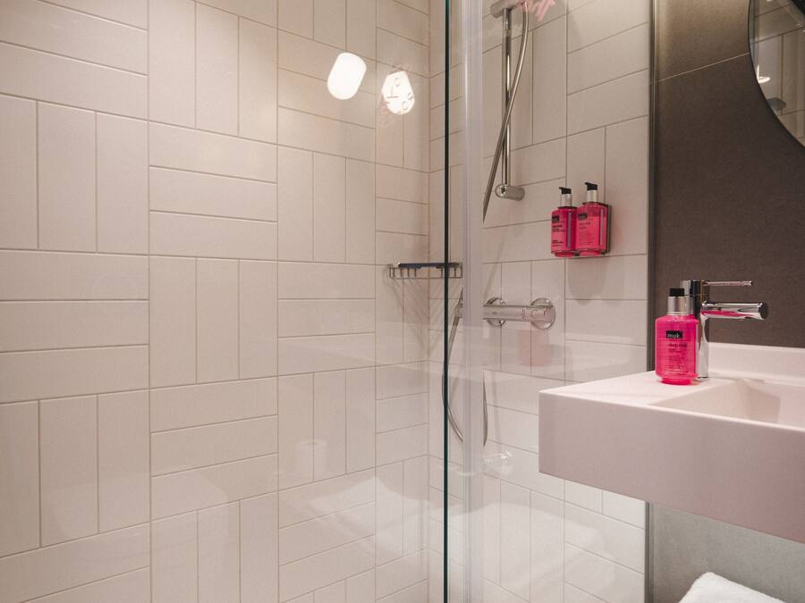 Un baño moderno con cabina de ducha de vidrio, azulejos blancos, lavamanos blanco y espejo.
