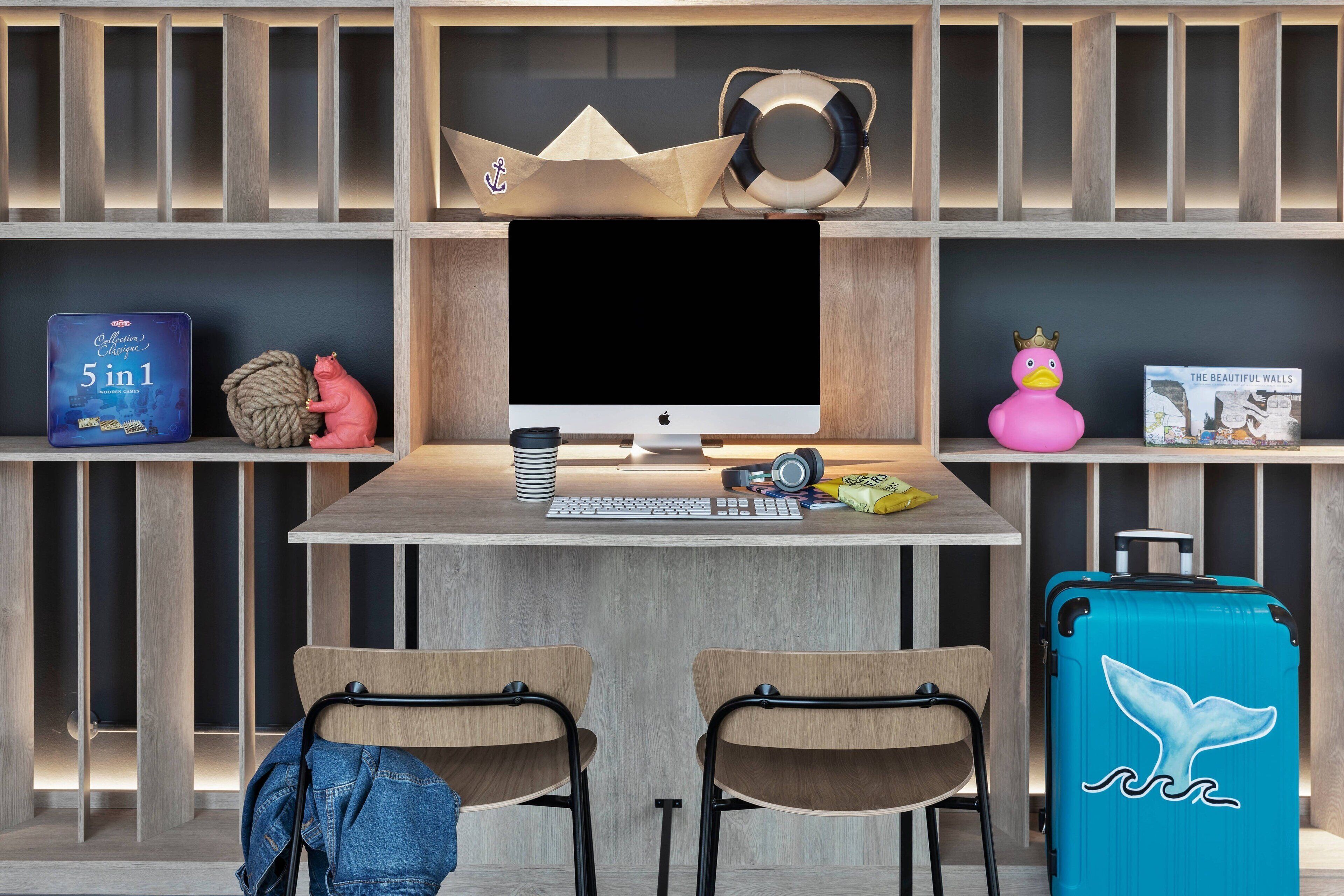 A modern workspace with a desk, two chairs, a computer, and a blue suitcase with a whale design.