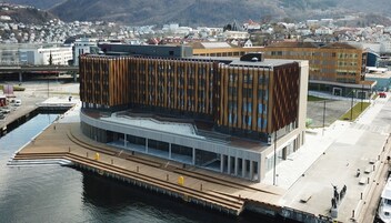 Un edificio moderno con una fachada de madera única, situado junto a la costa con un muelle que se adentra en el agua.
