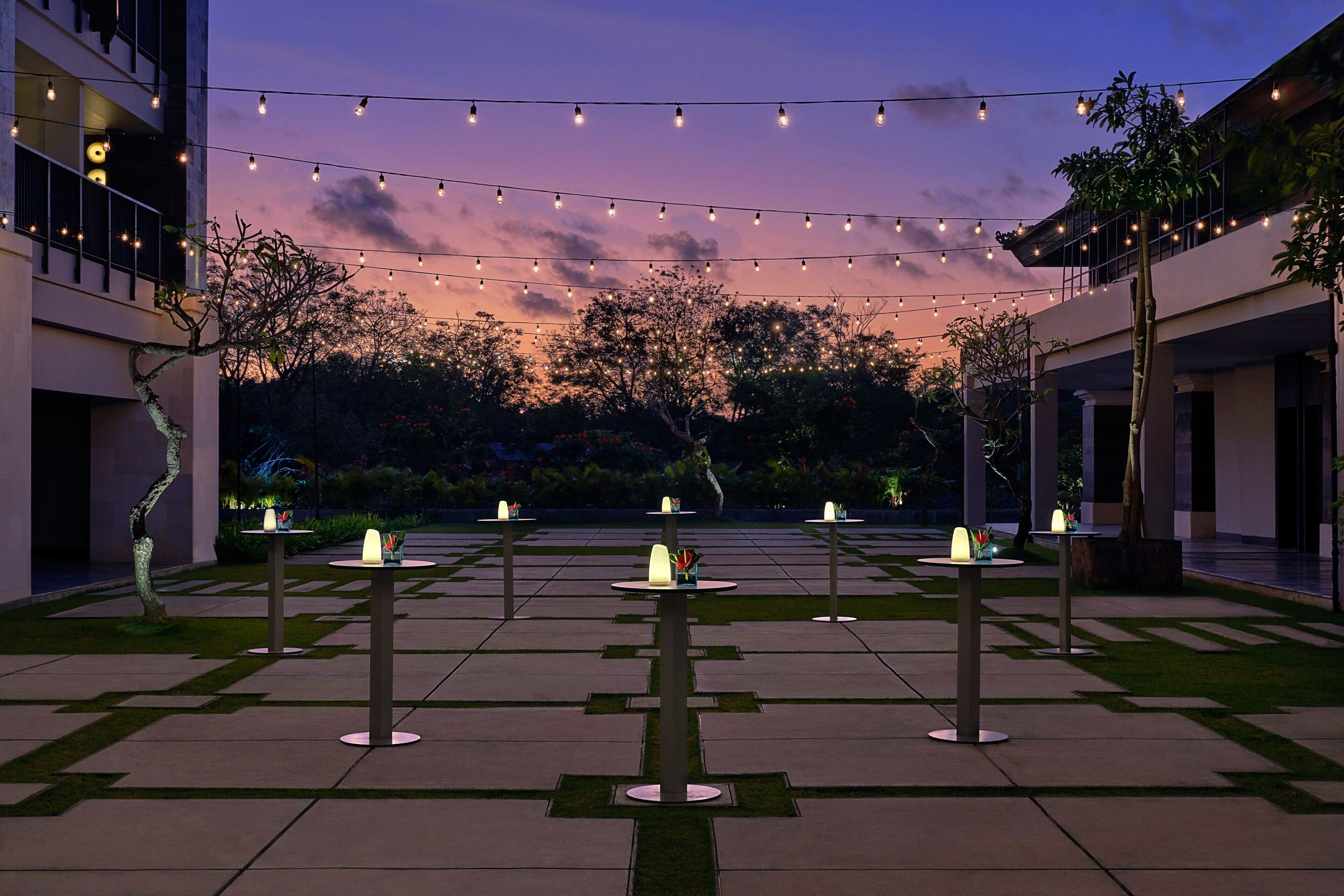 A courtyard with tables and chairs, string lights, and a sunset in the background.