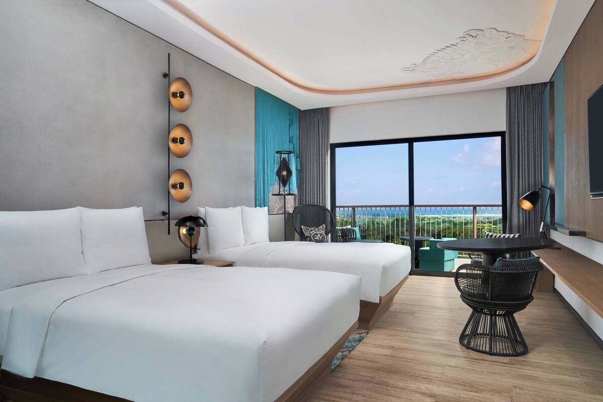 Habitación de hotel con dos camas, un balcón con vistas, una mesa redonda y un ventanal grande.