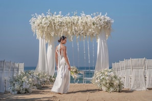 Decoración para una boda en la playa, con un arco floral blanco y asientos.