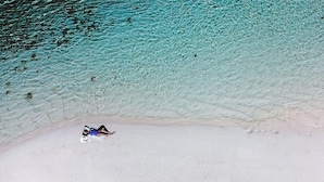 A person lying on a sandy beach with clear turquoise water. - Renaissance Bali Nusa Dua Resort (Nusa Dua)