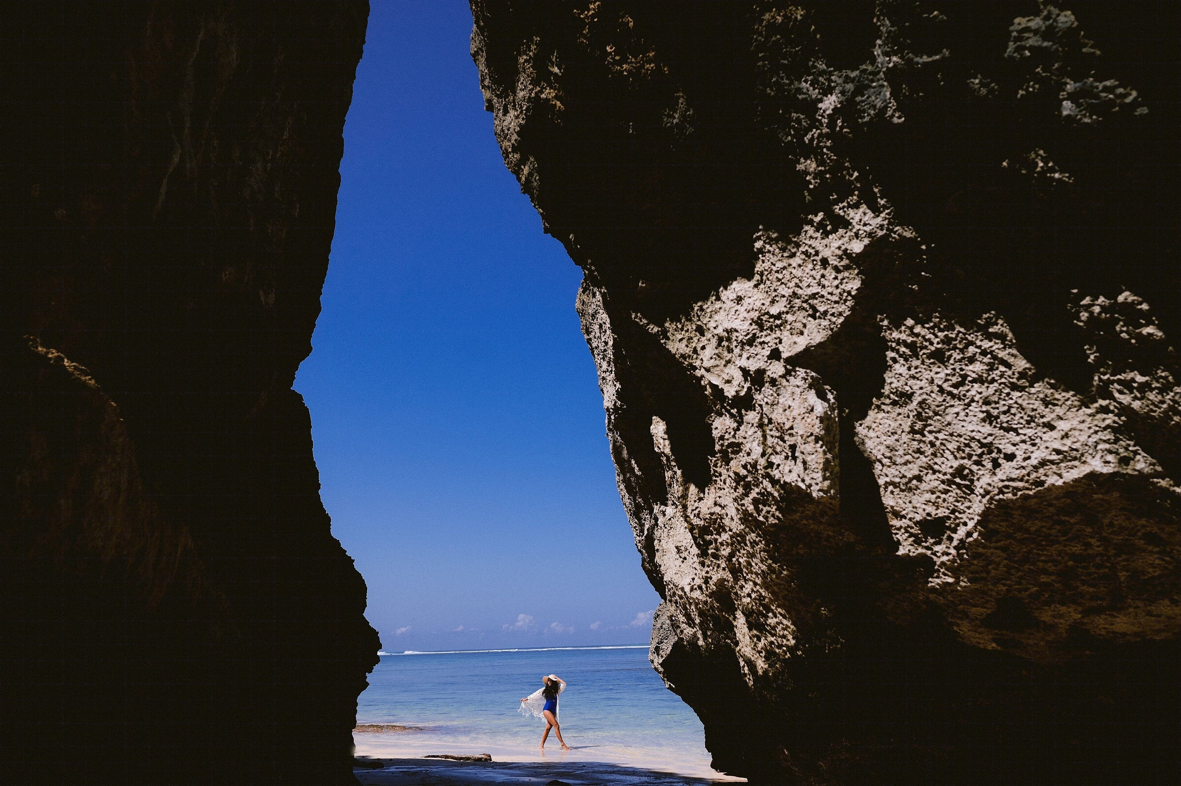 A person walking on a beach through a natural rock formation.