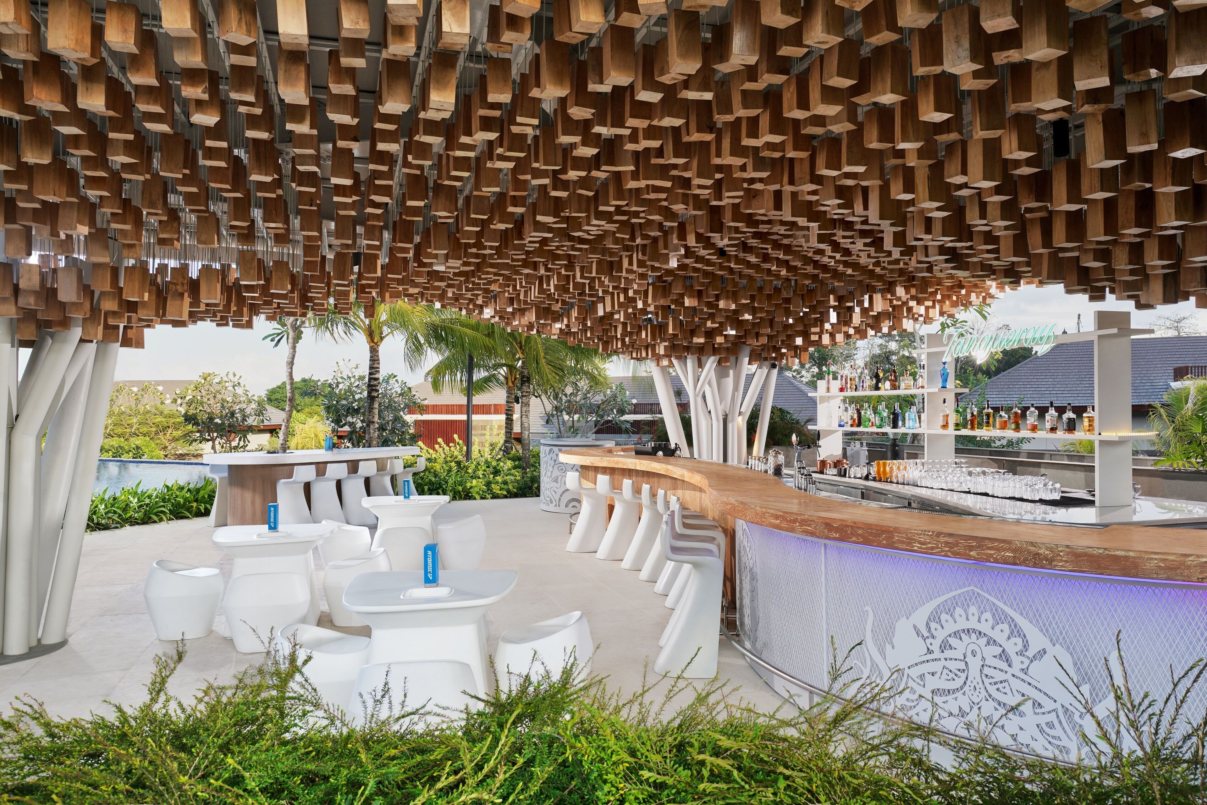 Een terras met witte stoelen en tafels, een houten balkenplafond en een bar met flessen.