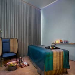 Relax in a comfortable seating area with a plush chair and side table, a neatly made bed, and a decorative vase arrangement.