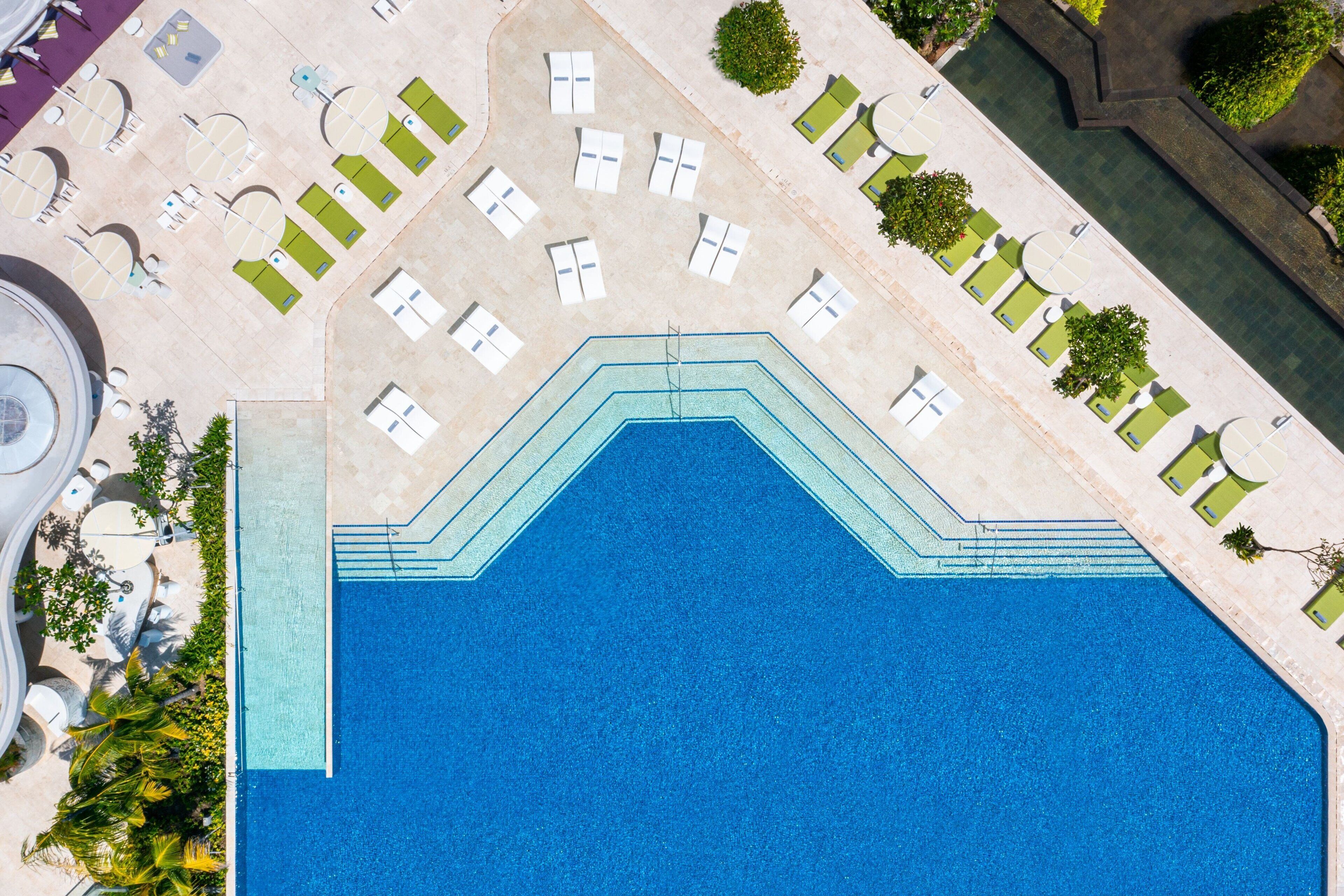 An aerial view of a swimming pool with multiple lanes, surrounded by lounge chairs and sunbeds.