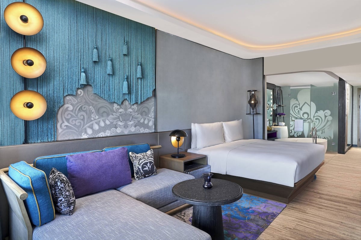 Una habitación de hotel moderna con sofá, cama, mesa redonda y una pared decorativa con luces colgantes.