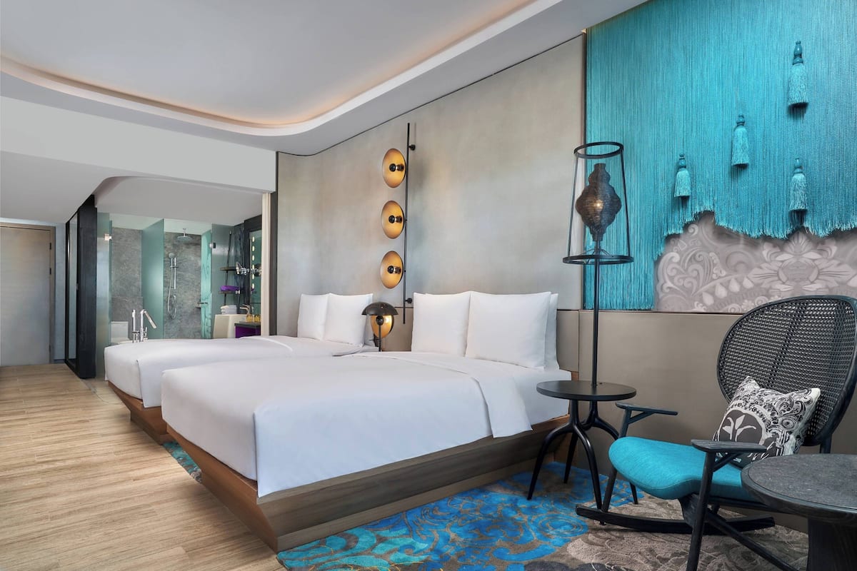 Una habitación de hotel moderna con una cama grande, una mesita pequeña, una silla y un detalle decorativo en la pared.
