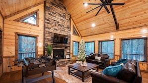 A cozy log cabin interior with a fireplace, a foosball table, leather sofas, and a Christmas tree. - High-End Romantic 1 Bedroom Cabin in highly sought after Timber Creek area (Broken Bow)