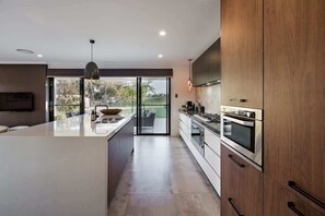 Een moderne keuken met een groot kookeiland, inbouwovens en een schuifdeur naar een balkon.
