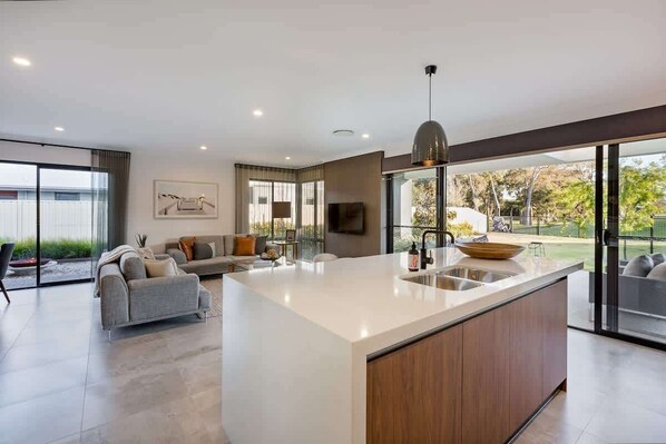 Een moderne keuken met een groot eiland, een zithoek met een bank, en uitzicht door grote ramen.