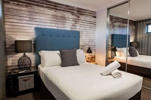 Een hotelkamer met een bed, een nachtkastje met een lamp, een spiegel en houten lambrisering.