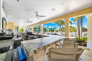 A bar area with a counter, seating, and a view of a pool and palm trees.