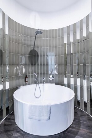 Een moderne badkamer met een groot vrijstaand bad, een handdouche en een wastafel aan de muur.