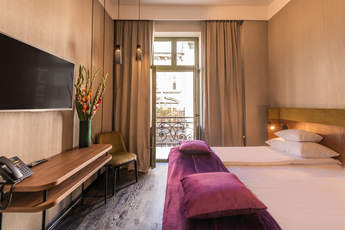 Une chambre d’hôtel avec un lit, un bureau avec un téléphone, une chaise, un téléviseur fixé au mur et une vue sur le balcon.