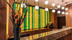 Een hotel receptie met een marmeren balie, een bloevas en een kleurrijk glas-in-loodraam.