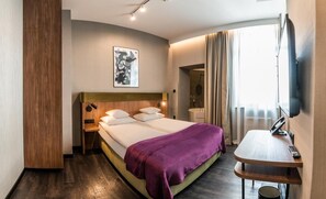 Een hotelkamer met een bed, nachtkastje, lamp, kunstwerk en een televisie.