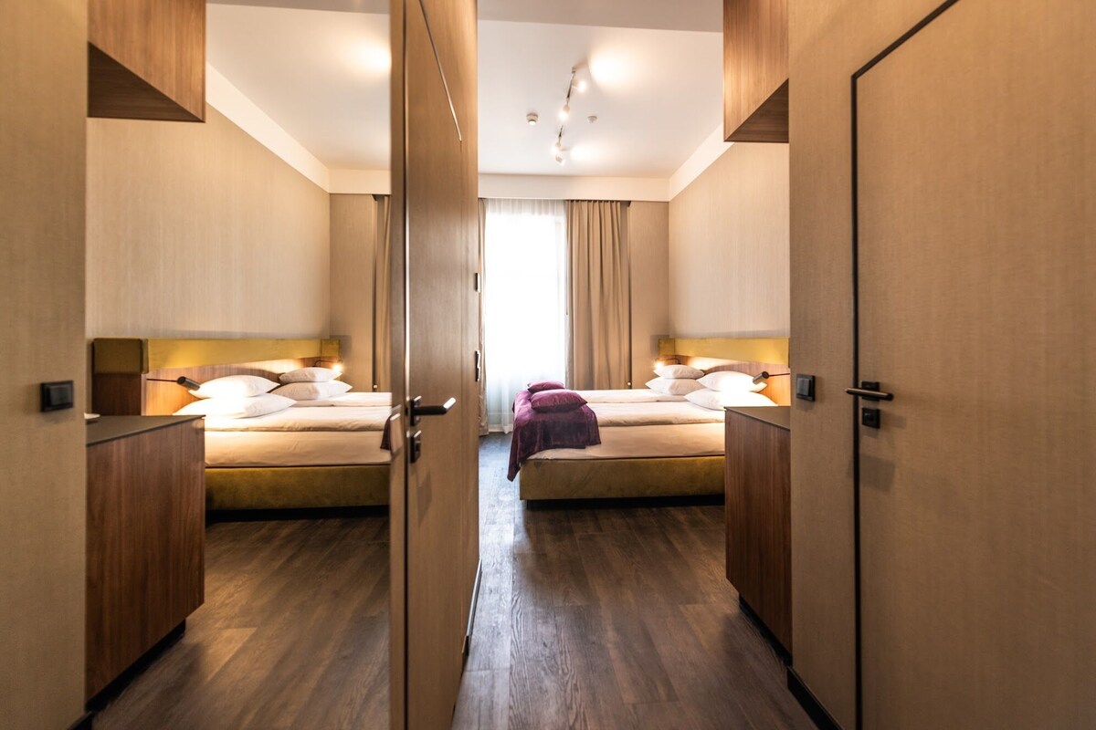 Une chambre d’hôtel avec deux lits, un plancher en bois et une décoration aux couleurs neutres.