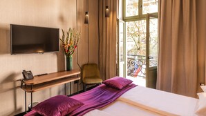 Een hotelkamer met een bed, een bureau met telefoon, een stoel, een aan de muur bevestigde televisie en een raam met gordijnen.