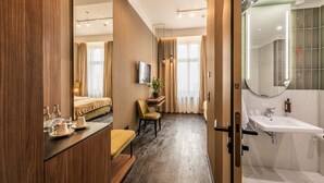 Een hotelkamer met een bed, nachtkastje, stoel en een badkamer met wastafel en spiegel.