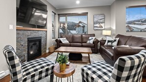 A modern living room with a fireplace, leather sofas, checkered chairs, and a large TV.