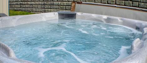A stone hot tub with a wooden bench and a metal container in the center.
