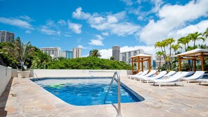 A swimming pool with lounge chairs and a cityscape in the background. - *Luana Waikiki*No Resort Fees* (Honolulu)