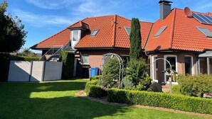 Une maison avec un toit recouvert de tuiles rouges, une cheminée et un jardin bien entretenu.