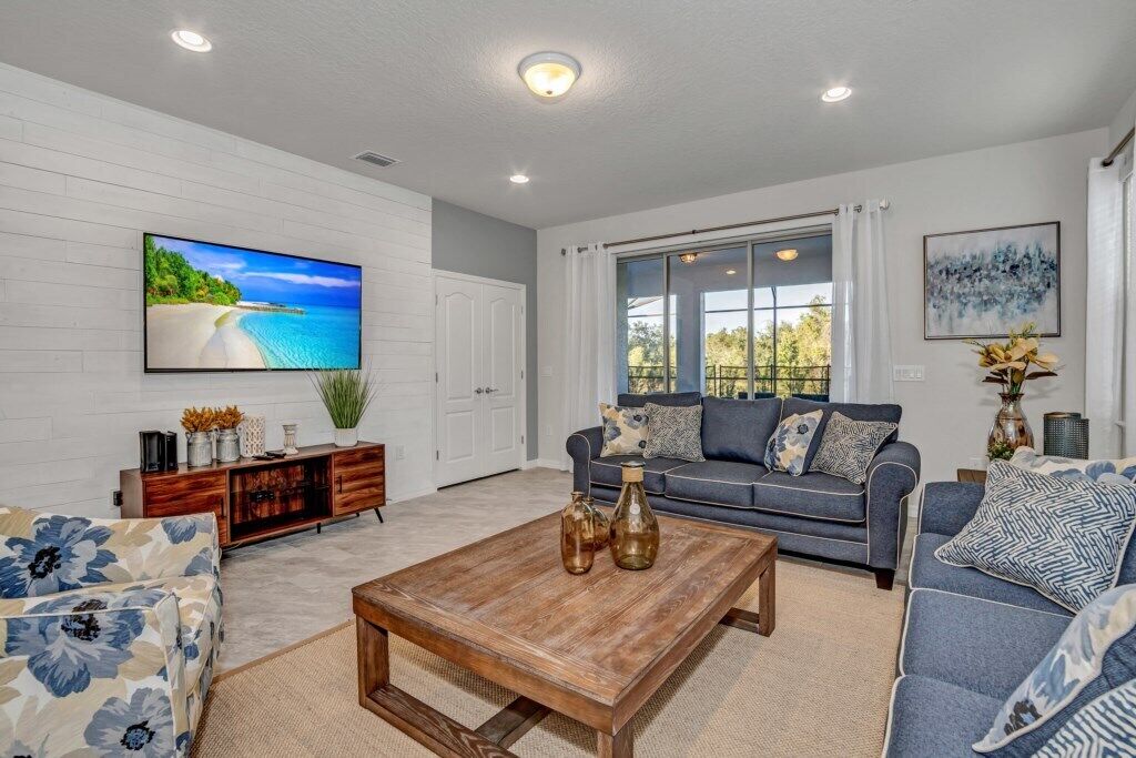 A living room with a large TV, a sofa, a coffee table, and a window with curtains.