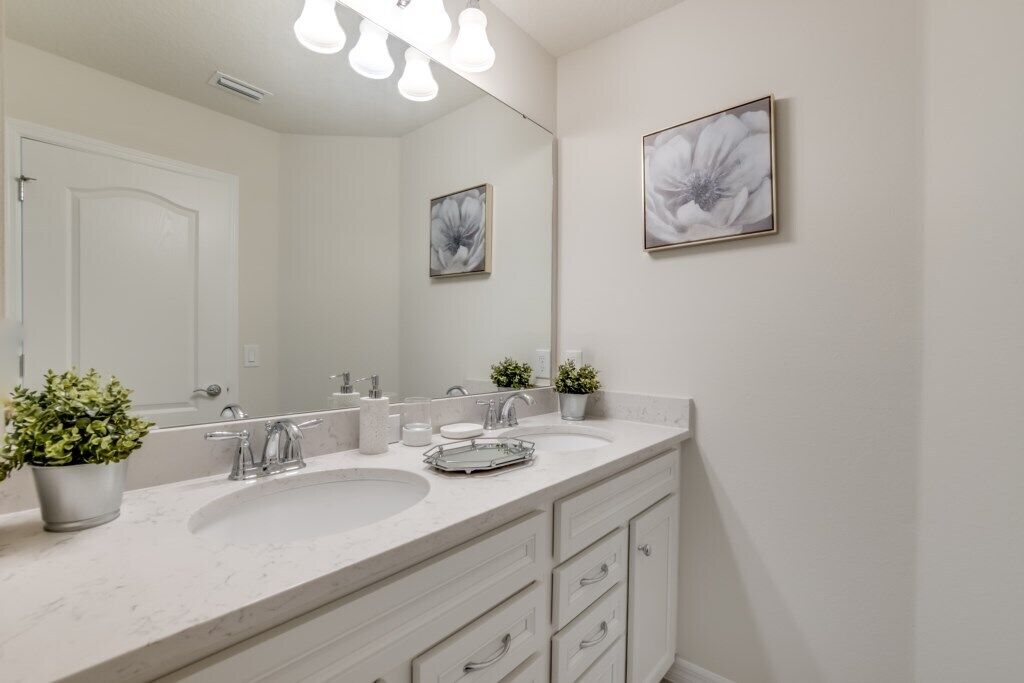 A bathroom with a white marble sink, two faucets, a large mirror, and a potted plant.