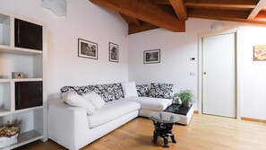 A living room with a white sofa, a glass coffee table, and a bookshelf. There are three framed pictures on the wall.