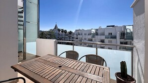 A balcony with a wooden table and chairs, a potted cactus, and a view of modern buildings. - R. MARINE II 434 Roses / Roses - INTERimmo (Rosas / Roses)