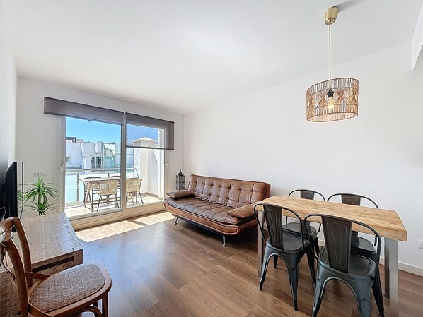 A spacious living area with a sofa, dining table, chairs, and a ceiling light fixture.