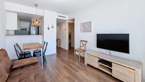 A modern living room with a flat-screen TV, wooden flooring, a dining area with a table and chairs, and a kitchen in the background. - R. MARINE II 434 Roses / Roses - INTERimmo (Rosas / Roses)
