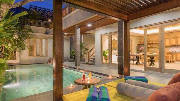 A poolside area with a wooden pergola, a seating area with cushions, and a view of the interior dining space. -  Villa Daun 2 Canggu by Premier Hospitality Asia (Canggu)