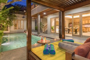 A poolside area with a wooden pergola, a seating area with cushions, and a view of the interior dining space. -  Villa Daun 2 Canggu by Premier Hospitality Asia (Canggu)