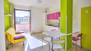 A small, brightly colored room with a dining table, chairs, a sofa, and a kitchen area. - Casa Pesca C: A modern and graceful apartment situated at a few steps from a sandy beach, with Free WI-FI. (Agropoli)