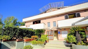 A two-story building with a central entrance, potted plants, and a clear sky. - Casa Pesca C: A modern and graceful apartment situated at a few steps from a sandy beach, with Free WI-FI. (Agropoli)