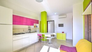 A compact kitchen with white cabinets, a pink upper section, and a green accent wall. There is a dining area with a white table and chairs, and a yellow sofa with a purple cushion. - Casa Pesca C: A modern and graceful apartment situated at a few steps from a sandy beach, with Free WI-FI. (Agropoli)