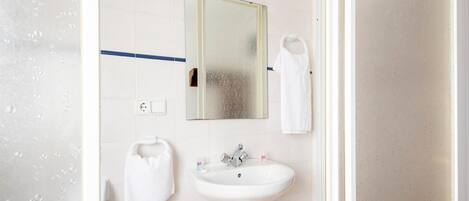 Un baño con lavamanos blanco, un espejo y un perchero para toallas.