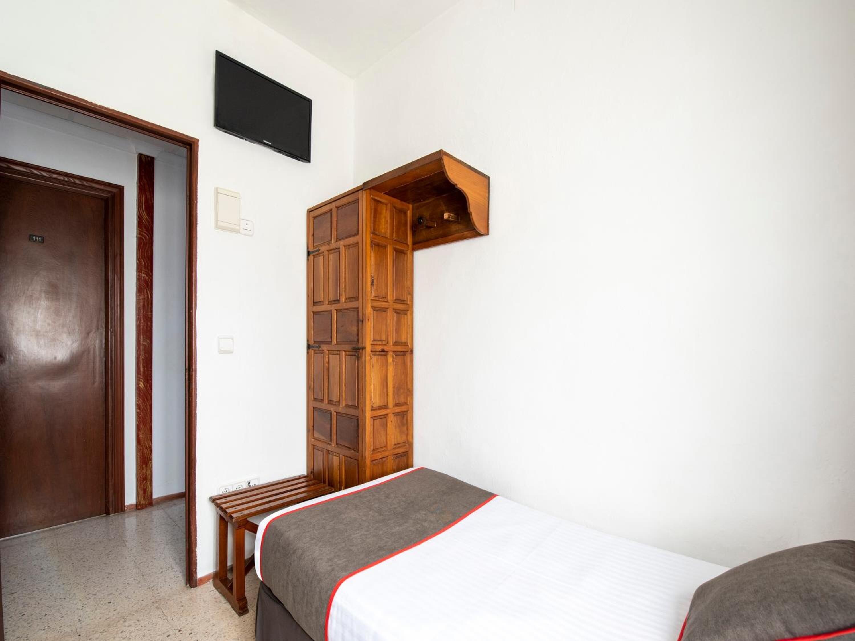 Una stanza piccola e modesta con un letto, un armadietto in legno, una TV e una porta.