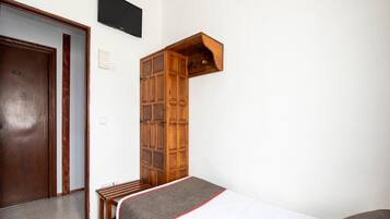 Una stanza piccola e modesta con un letto, un armadietto in legno, una TV e una porta.