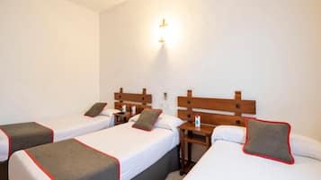 Une chambre d’hôtel avec trois lits simples, chacun doté d’une tête de lit en bois et d’une touche de couleur rouge et grise. Chaque lit est agrémenté d’une table de chevet sur laquelle se trouvent une bouteille et un verre.