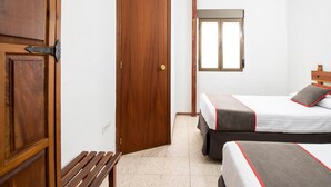 Een hotelkamer met twee bedden, een houten bankje, een deur en een raam.